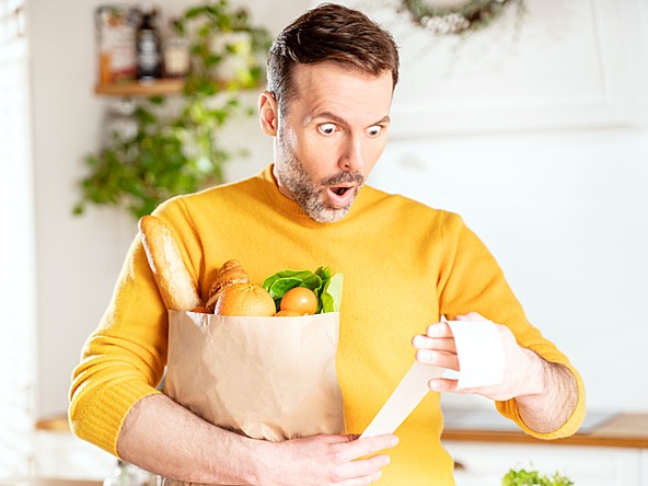 Man looking shocked at food prices on supermarket receipt